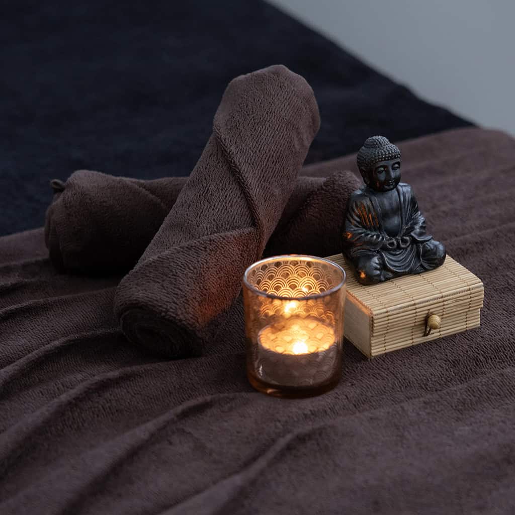 table de massage avec des serviettes bordeaux, bougie et une statue de bouddha posée dessus